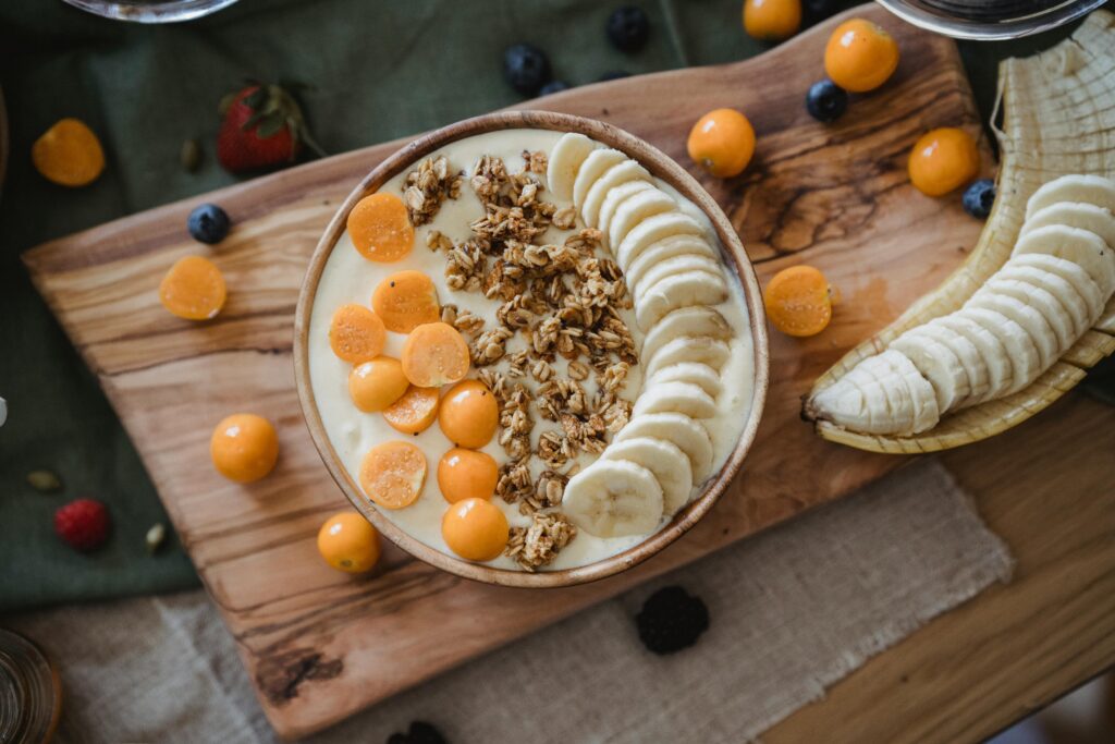 Top view of a wooden bowl with bananas, granola, and golden berries.