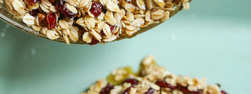 Close-up of homemade granola with oats and cranberries pouring from a bowl.
